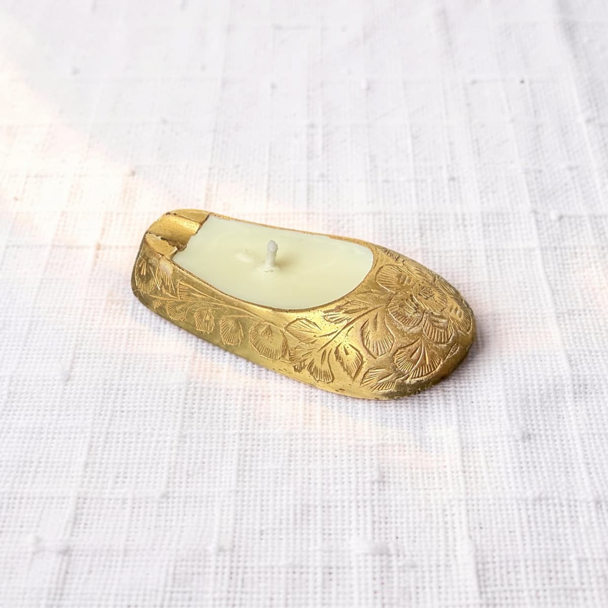Decorative brass candle holder with a white candle on a textured white fabric background