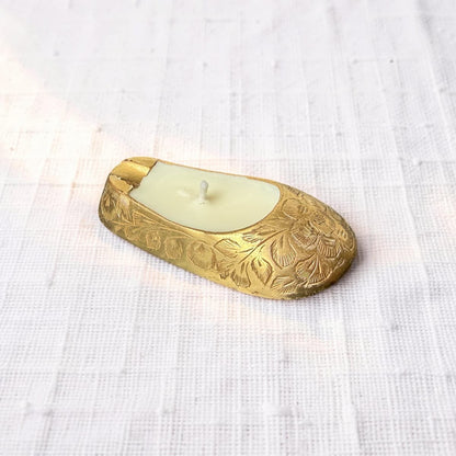 Decorative brass candle holder with a white candle on a textured white fabric background