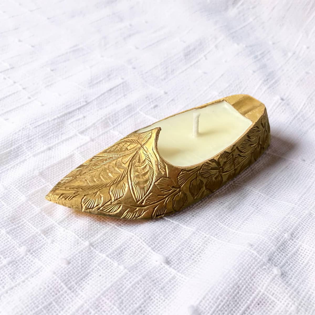 Decorative gold candle holder with a white candle on a white textured surface