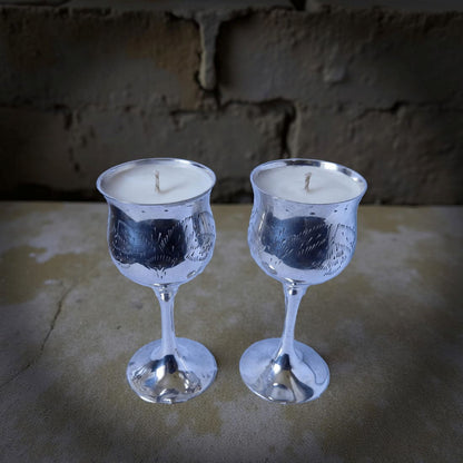 Two silver candle holders with candles inside on a stone surface.