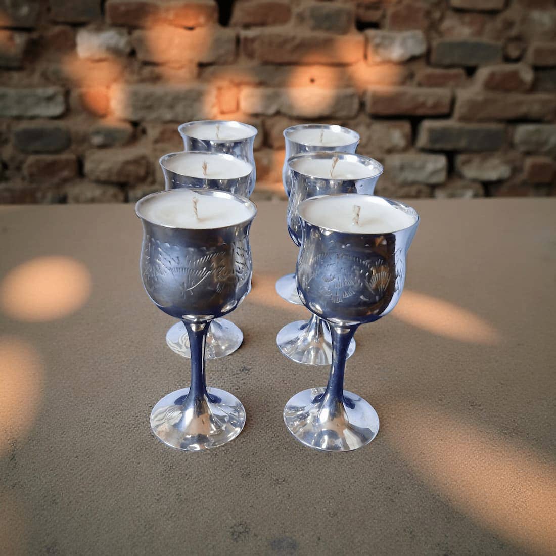 Silver wine glass candles on a stone surface with a brick wall background