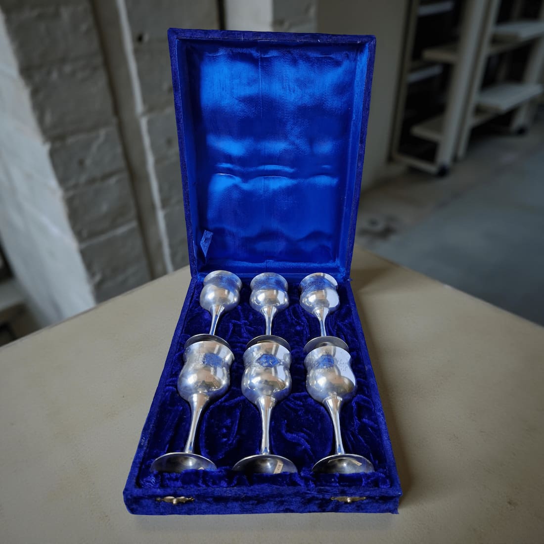 Set of silver ladles in a blue velvet box on a wooden surface.