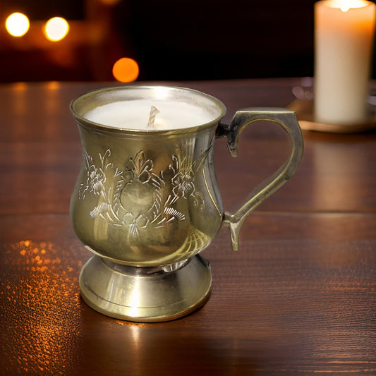 Decorative brass mug with a candle inside on a wooden surface.