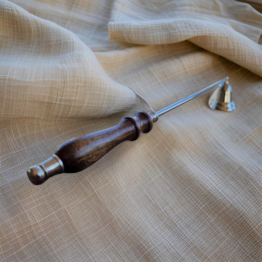 Candle snuffer with wooden handle and metal prongs on a textured fabric background