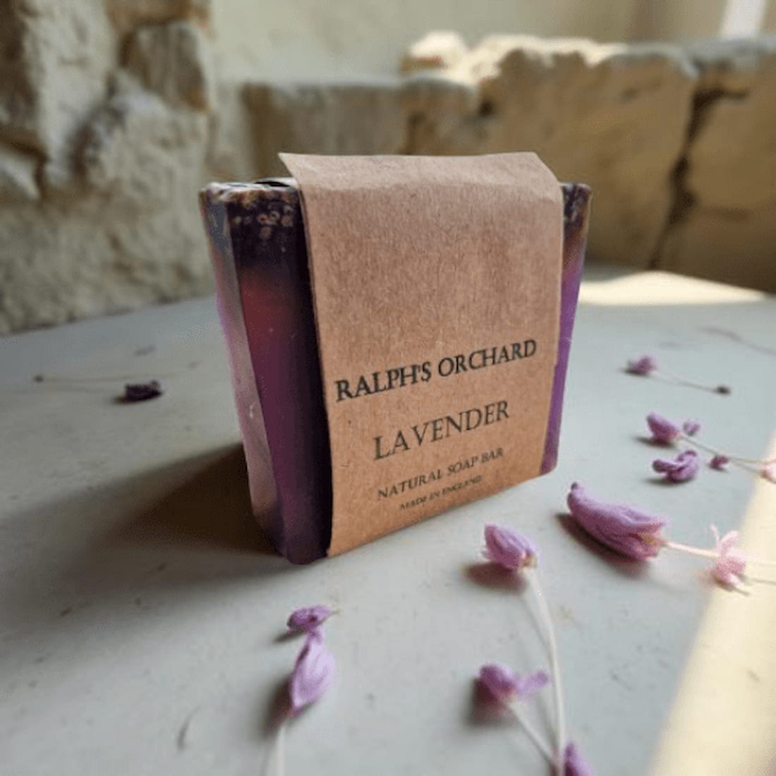 Lavender soap bar with a brown paper label on a stone surface with lavender flowers.