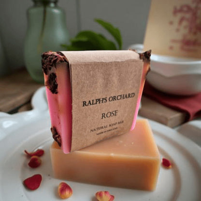 Bar of soap with 'Ralph's Orchard' branding on a white plate with rose petals.