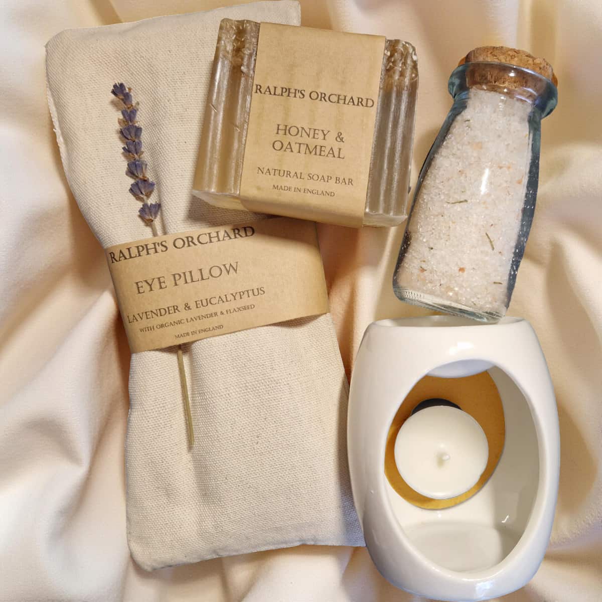 Ralph's Orchard products including a soap bar, eye pillow, and candle on a soft fabric background