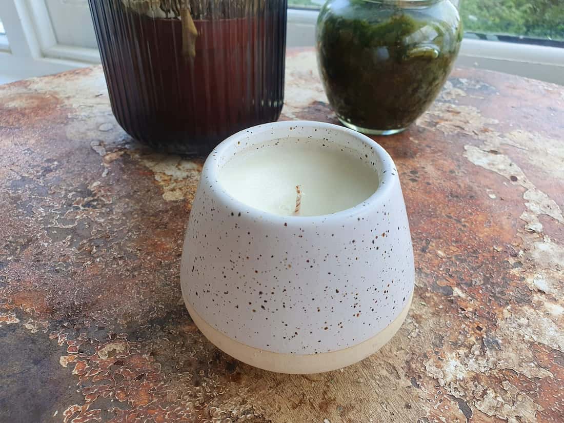 Speckled ceramic candle holder on a textured surface with jars in the background