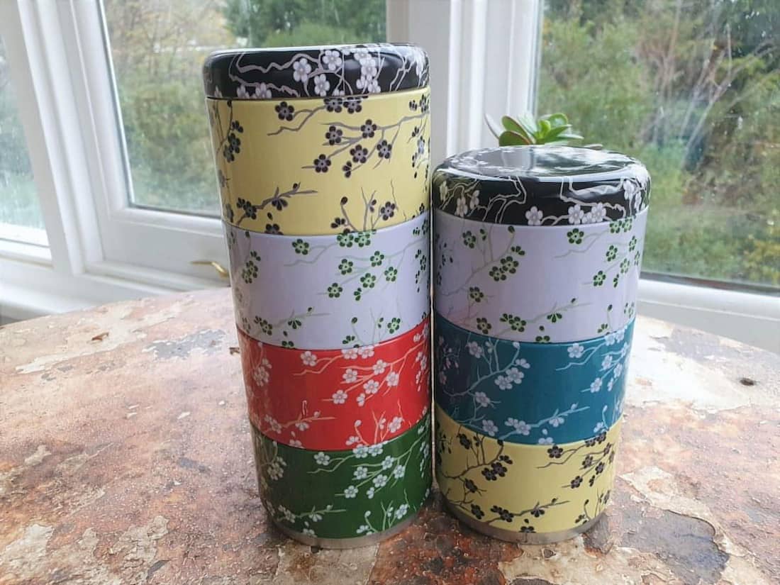 Two cylindrical containers with floral patterns on a surface near a window.