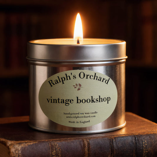 Candle in a metal tin labeled 'Ralph's Orchard vintage bookshop' on an old book.