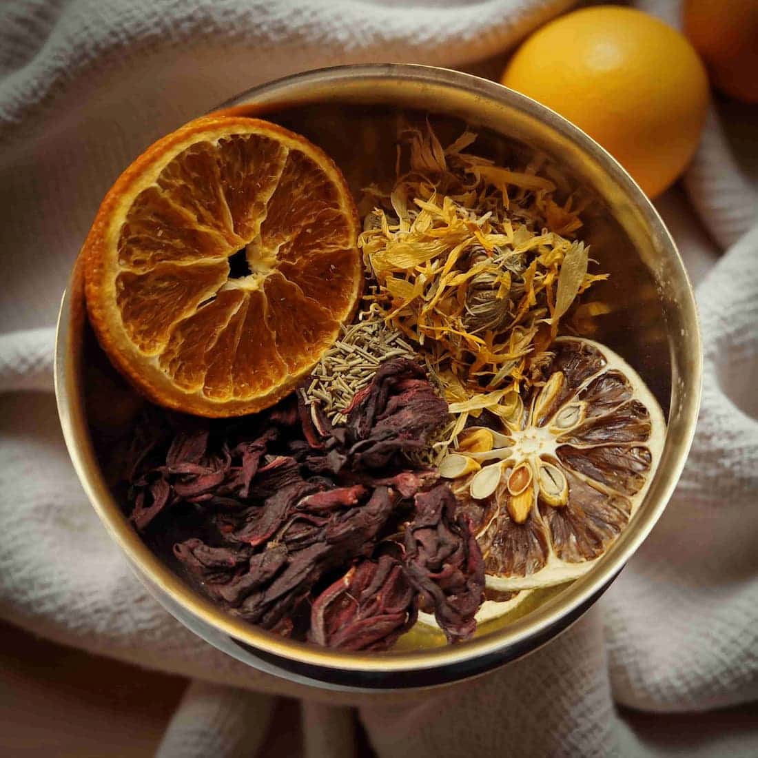 Spice blend with dried oranges, lemons, and herbs in a metal container.