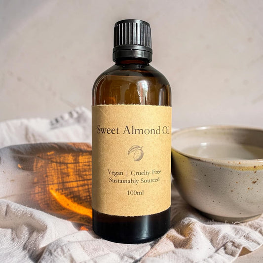 Bottle of Sweet Almond Oil with a label, placed on a textured surface with a bowl and wooden block in the background.