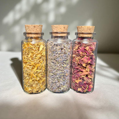 Three glass jars with cork lids containing dried herbs on a light surface.