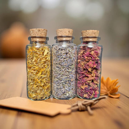Three glass jars with cork lids containing dried herbs on a wooden surface.