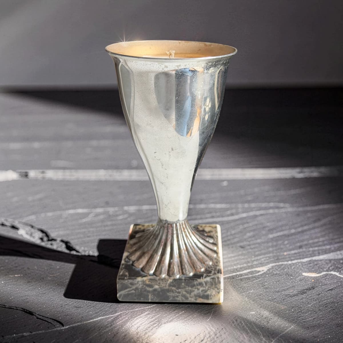 Silver candle holder on a textured surface with a dark background
