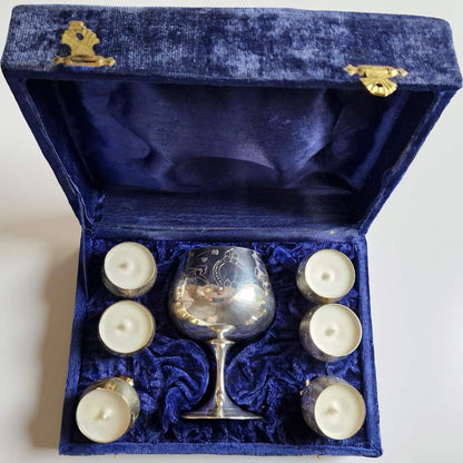 Silver goblet and six white candles in a blue velvet box on a white background