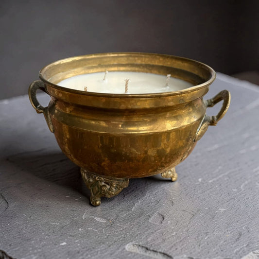 A five-wick brass candle in an ornate, vintage-style bowl with side handles and a small footed base, resting on a dark gray slate surface against a dark gray background.