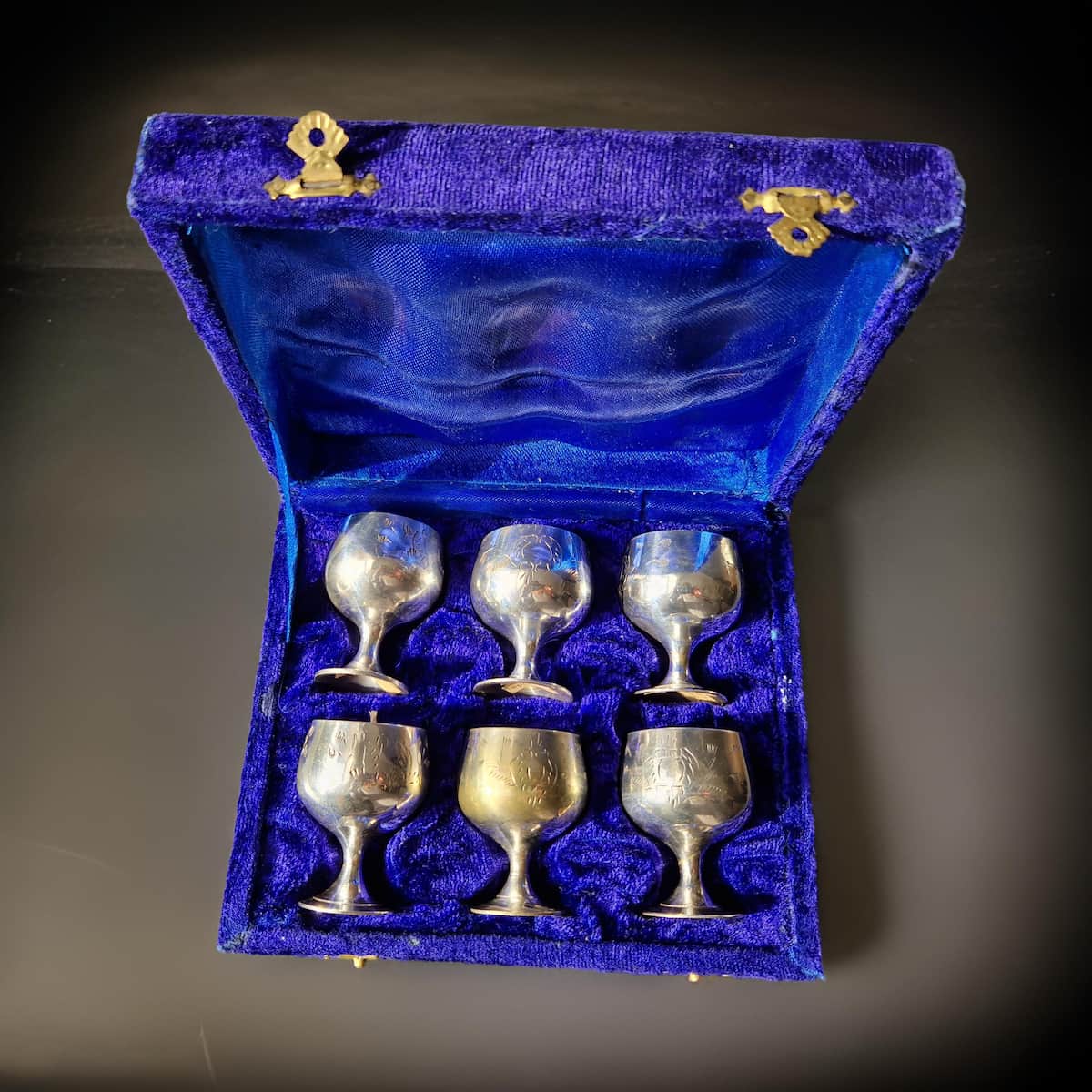 Set of six silver goblets in a blue velvet box on a dark background