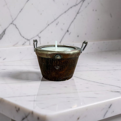 A small metal candle holder with a white wax candle, set on a white marble surface against a matching marble background.