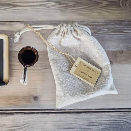 Textile bag with a tag labeled 'Tomato Leaf' on a wooden surface with a cup of coffee and phone.