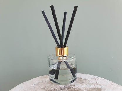 reed diffuser with thick black reeds, plants in backrgound